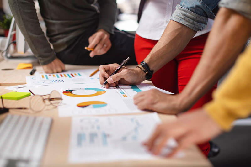 closeup on group of hands at desktop with marketing materials